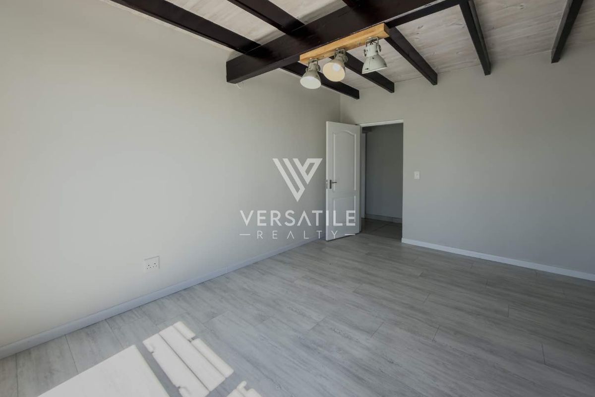 A bright, empty bedroom featuring modern laminate flooring, exposed timber ceiling beams, and contemporary track lighting.