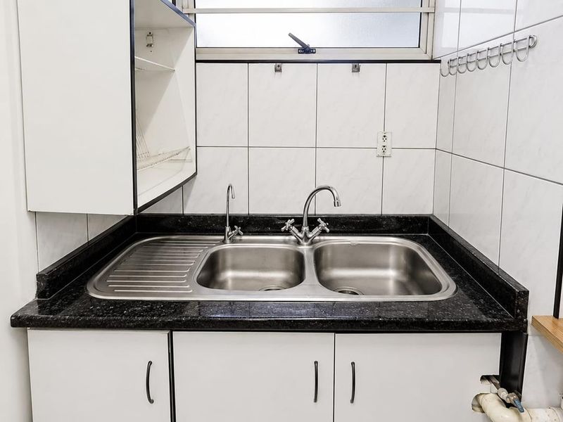 A functional scullery area featuring a stainless steel double sink, granite countertop, and white built-in cabinetry with tiled wall finishes.