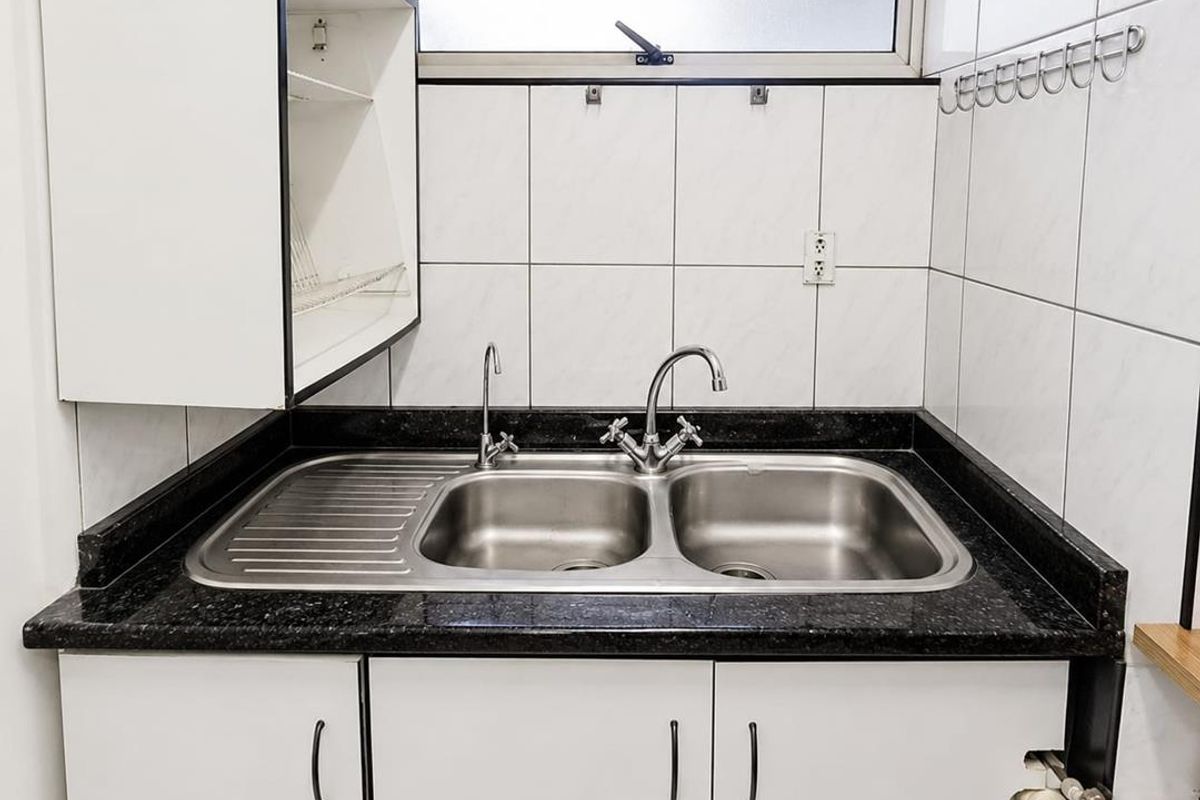 A functional scullery area featuring a stainless steel double sink, granite countertop, and white built-in cabinetry with tiled wall finishes.