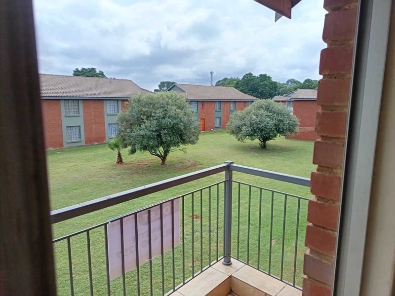 A balcony with a metal balustrade overlooking a communal garden area within the apartment complex.