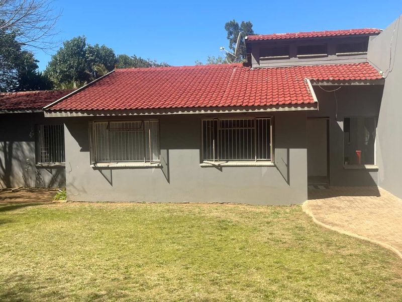 Rear view of the house featuring a terracotta tiled roof, security bars on windows, and a paved walkway leading to the entrance.