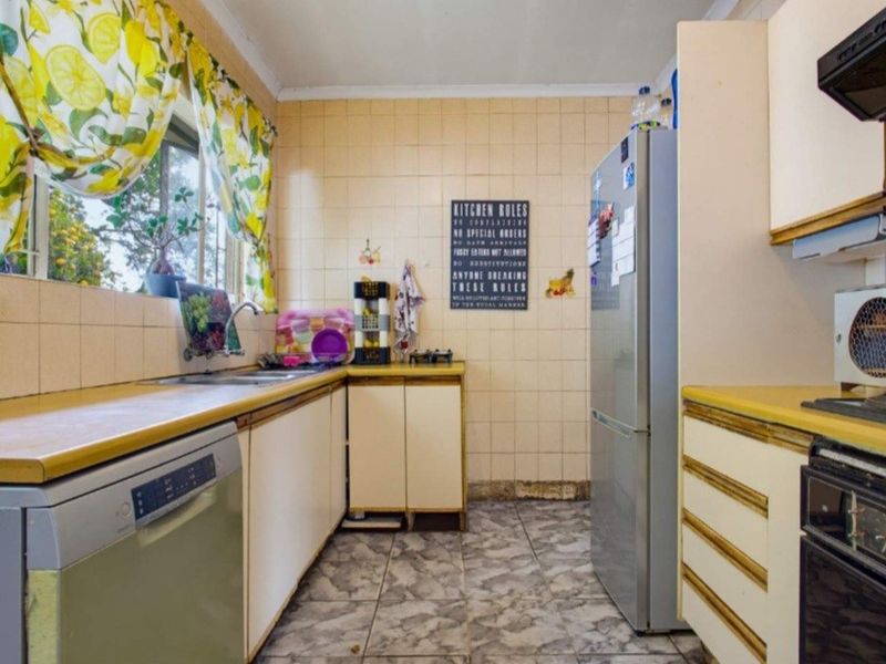 A dated kitchen featuring laminate countertops, tiled splashbacks, and built-in cabinetry, offering potential for a modern renovation.