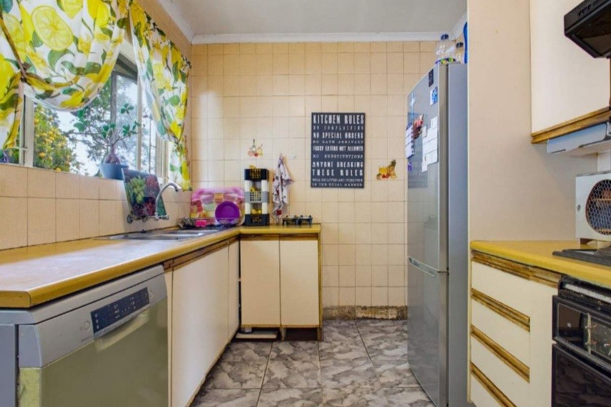 A dated kitchen featuring laminate countertops, tiled splashbacks, and built-in cabinetry, offering potential for a modern renovation.