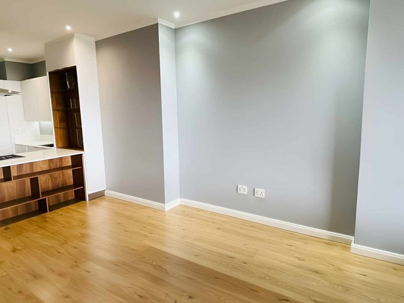 Modern open-plan living area featuring light wood-look laminate flooring, neutral grey walls, and a sleek kitchen with integrated cabinetry and stone countertops.
