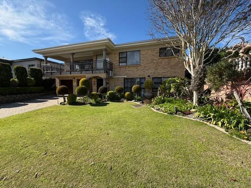 A two-story brick residential property featuring an upper-level balcony, paved driveway, and a well-maintained front garden.