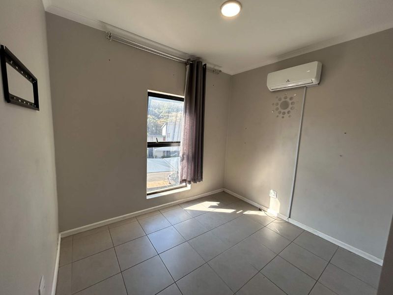 A vacant bedroom featuring tiled flooring, a wall-mounted split-system air conditioner, and a window with a curtain rail.