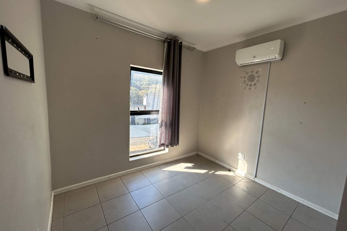 A vacant bedroom featuring tiled flooring, a wall-mounted split-system air conditioner, and a window with a curtain rail.