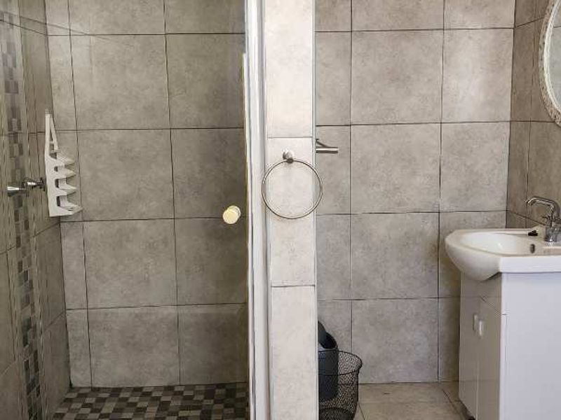 A functional bathroom featuring a glass-enclosed shower, a vanity basin, and neutral floor-to-ceiling tiling throughout.