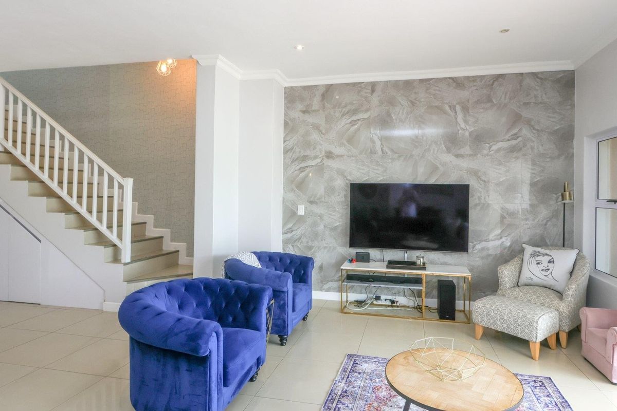 A bright living room featuring a modern marble-effect feature wall, tiled flooring, and an integrated staircase with white balustrades.