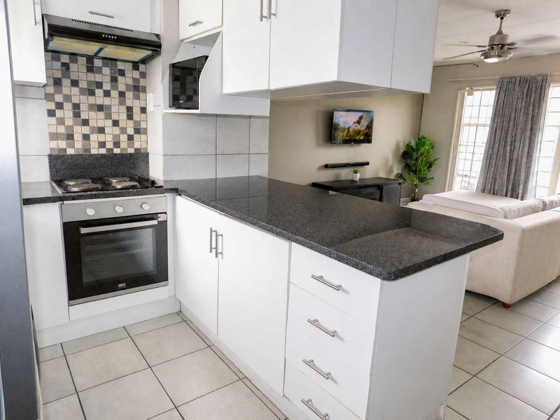 Open-plan kitchen featuring white cabinetry, granite countertops, and a mosaic backsplash, seamlessly flowing into the adjacent living area with tiled flooring throughout.