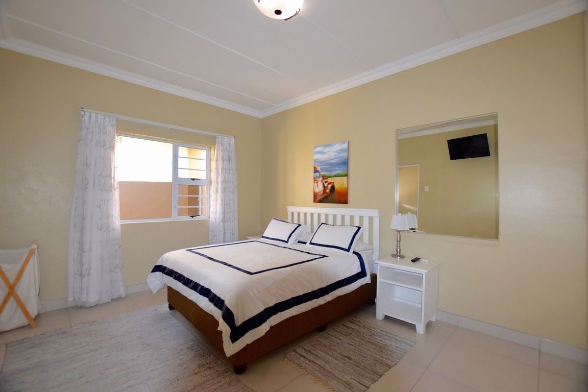 A well-lit bedroom featuring tiled flooring, crown molding, and a large wall-mounted mirror.
