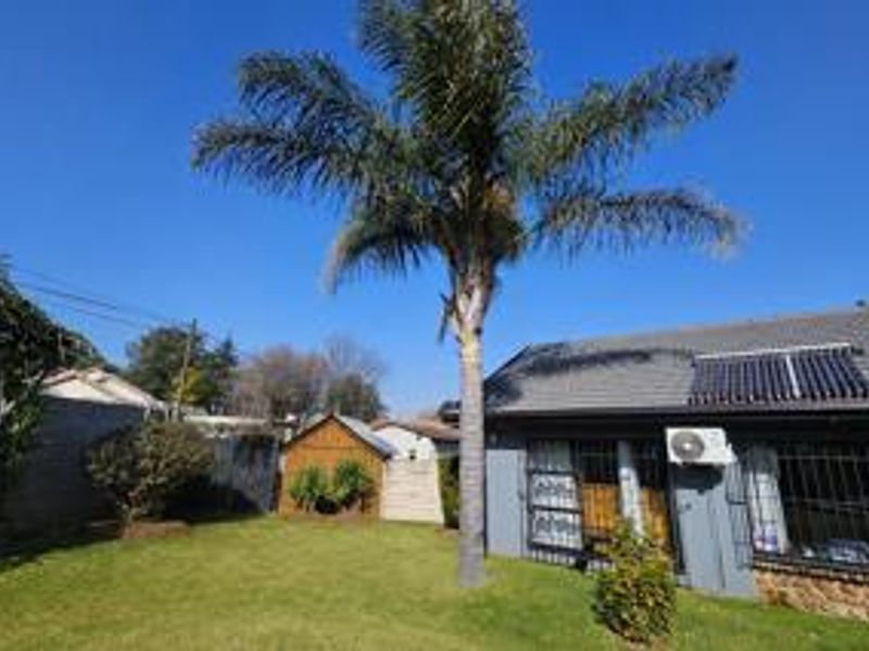 Rear exterior view of the property featuring a lawn, mature palm tree, solar water heating panels, and an external air conditioning unit.