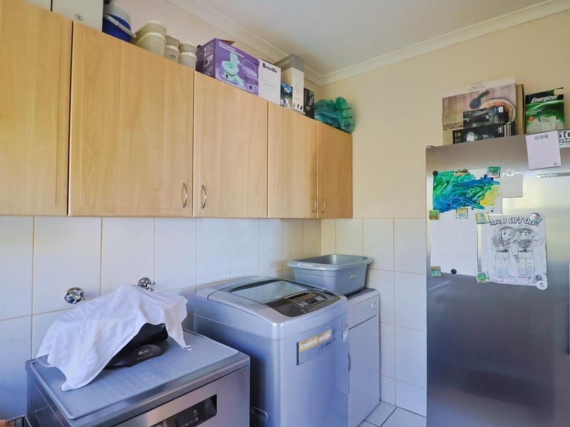 A functional laundry room featuring built-in cabinetry, tiled splashbacks, and dedicated plumbing connections for washing appliances.