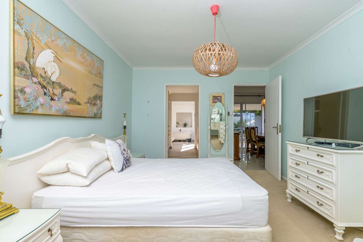 A well-lit bedroom featuring neutral carpeting, light blue walls, and direct access to an adjoining bathroom and living area.