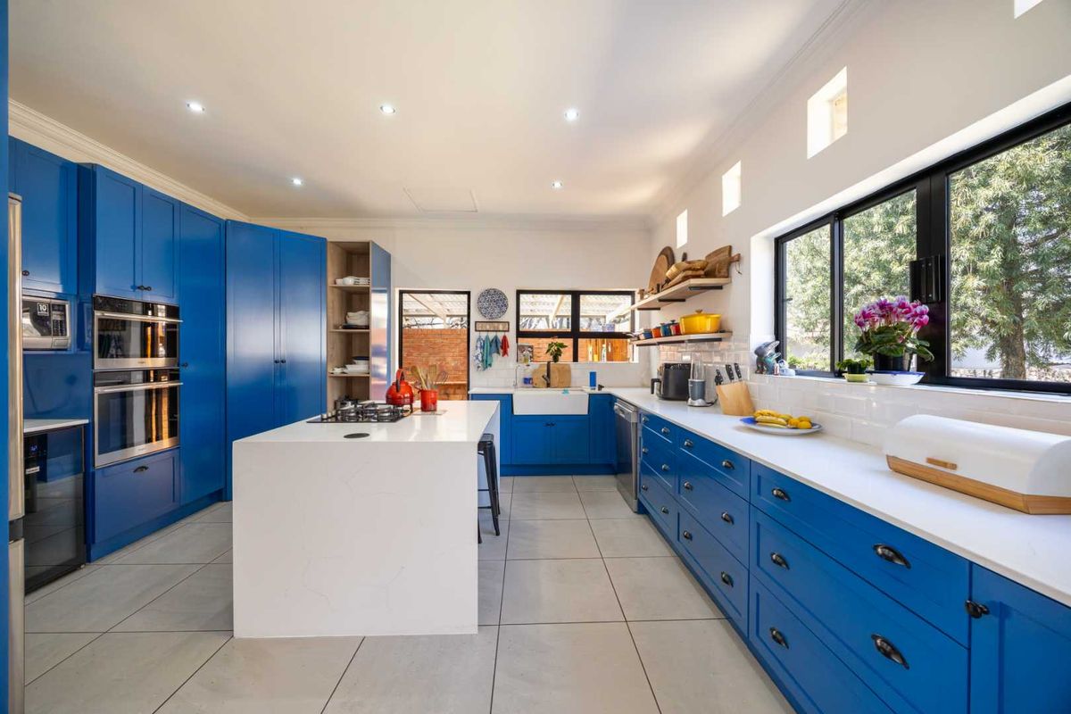 Modern kitchen featuring vibrant blue cabinetry, a central island with a gas cooktop, quartz countertops, and a farmhouse sink with subway tile backsplash.