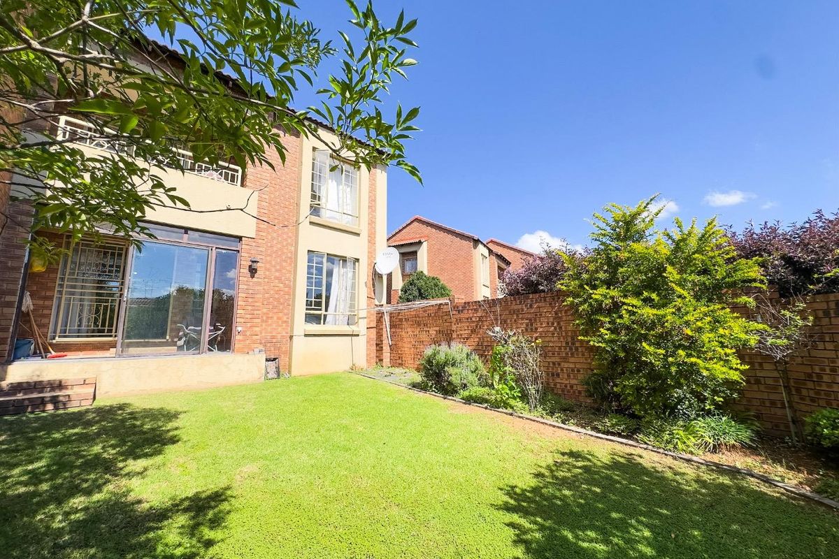 A private rear garden featuring a well-maintained lawn, brick boundary walls, and access to the townhouse via sliding glass doors and a balcony.