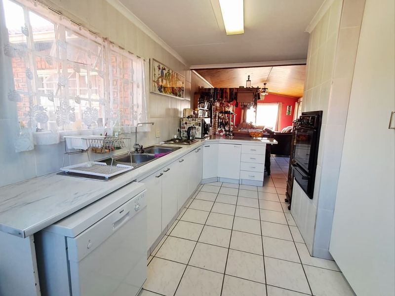 A functional kitchen featuring white cabinetry, tiled flooring, a double basin sink, and a built-in oven, with an open-plan flow to the living area.