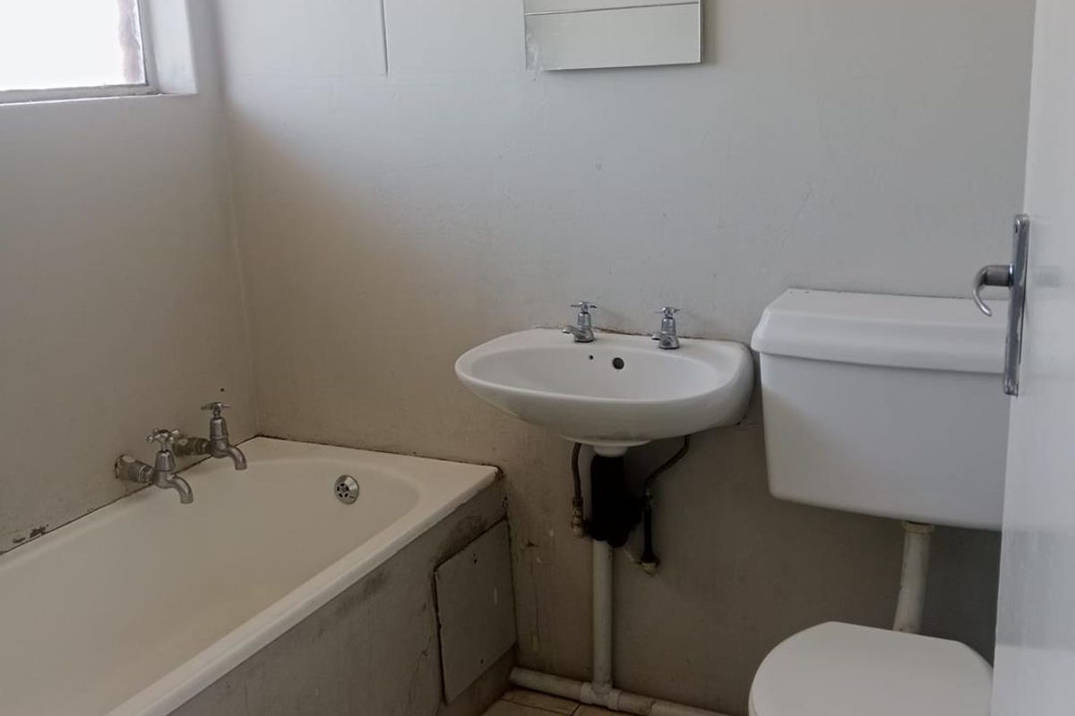 A dated bathroom featuring a standard bathtub, pedestal basin, and toilet, requiring cosmetic updates and floor tile repairs.
