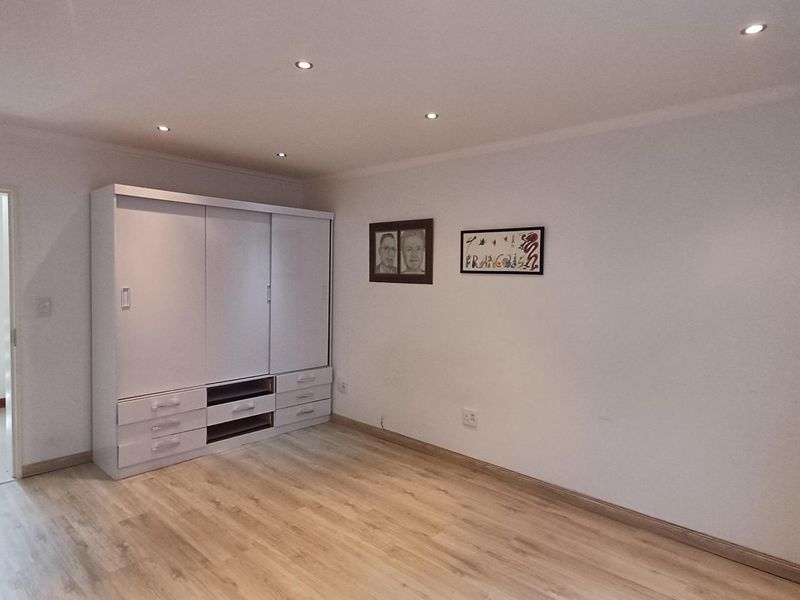 A well-maintained bedroom featuring light-toned laminate flooring, recessed ceiling downlights, and a large built-in wardrobe with sliding doors.