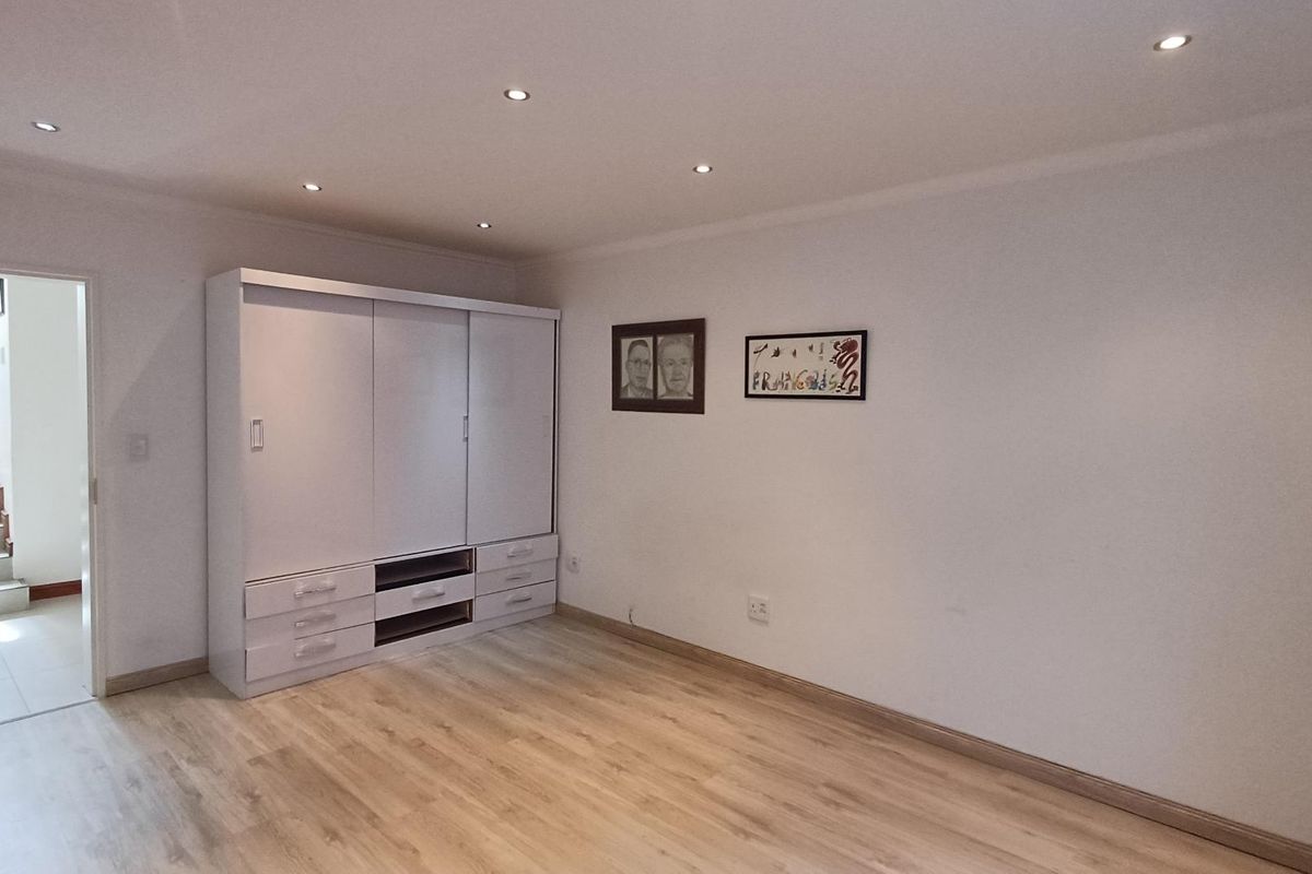 A well-maintained bedroom featuring light-toned laminate flooring, recessed ceiling downlights, and a large built-in wardrobe with sliding doors.