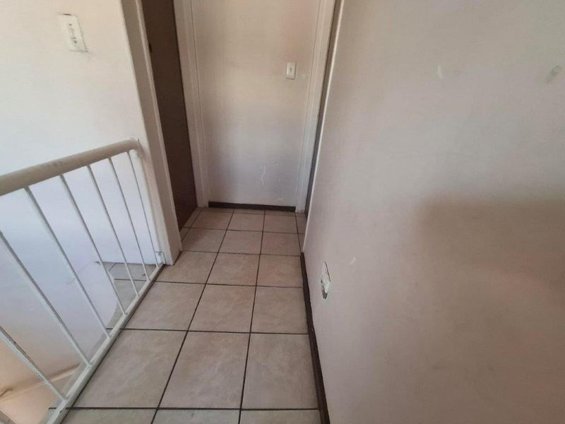A functional hallway area featuring tiled flooring and a metal balustrade overlooking the staircase, requiring minor cosmetic updates to the wall finishes.