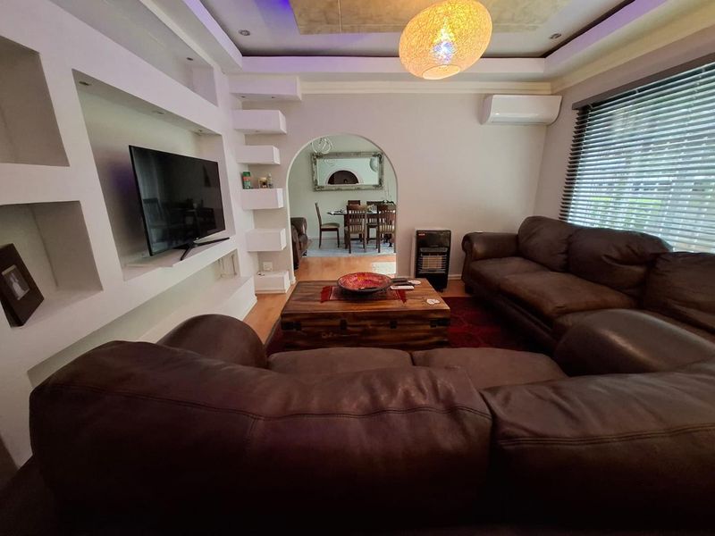 A comfortable living room featuring built-in shelving, recessed ceiling lighting, and an archway leading to the dining area, equipped with a split-system air conditioner.