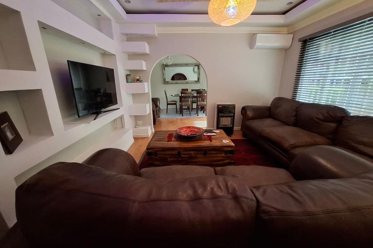 A comfortable living room featuring built-in shelving, recessed ceiling lighting, and an archway leading to the dining area, equipped with a split-system air conditioner.