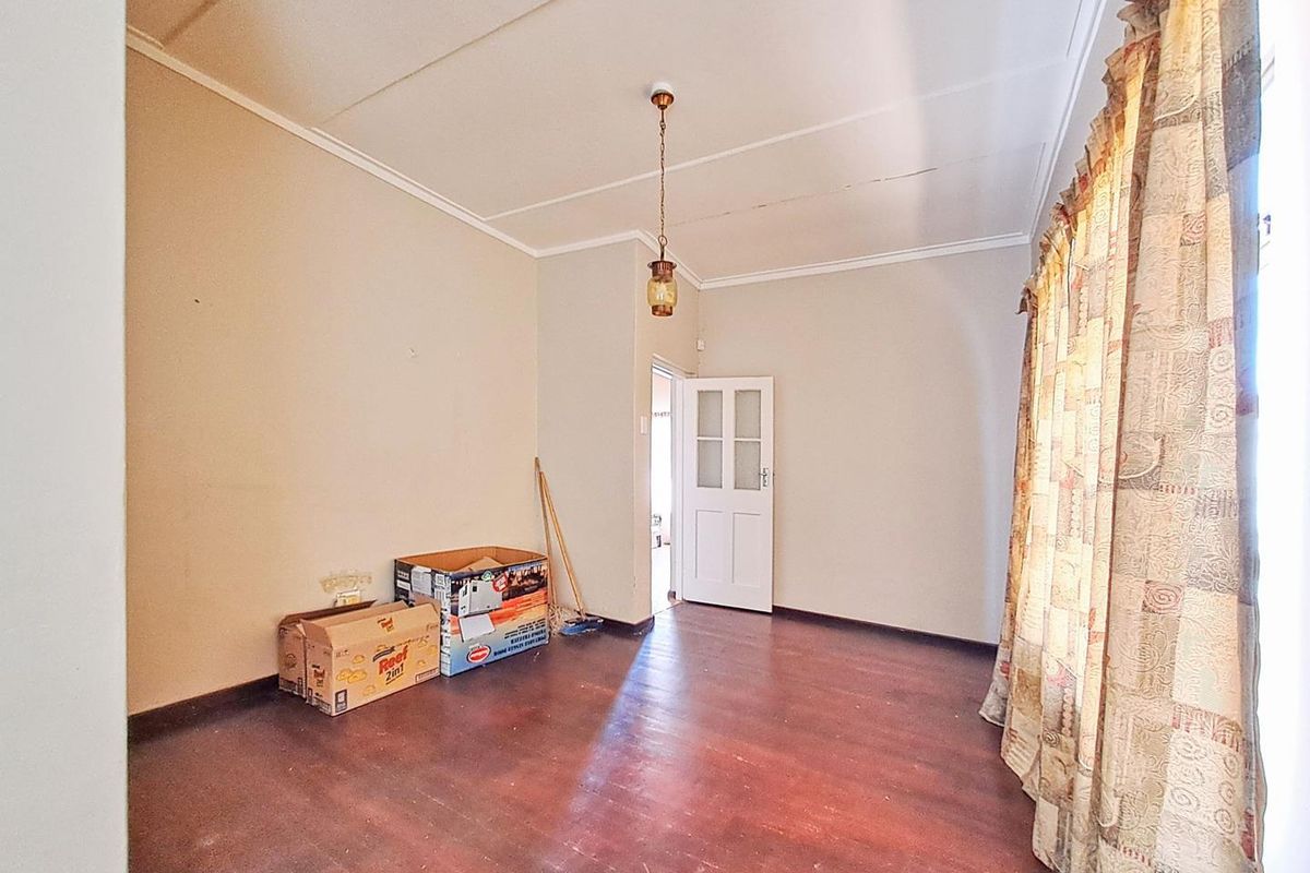 A vacant bedroom featuring dark wood-look flooring, neutral walls, and a classic pendant light fixture.