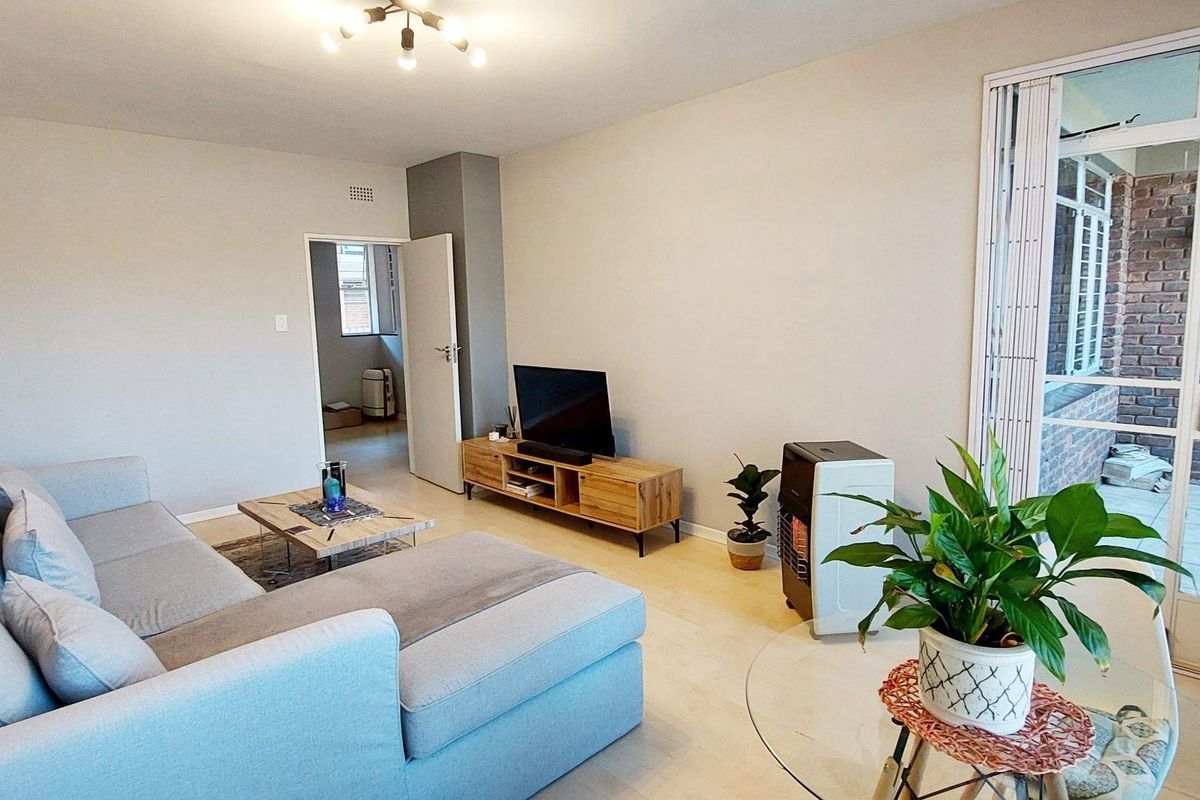 A bright and spacious living room featuring light laminate flooring and a sliding glass door providing access to an outdoor patio area.