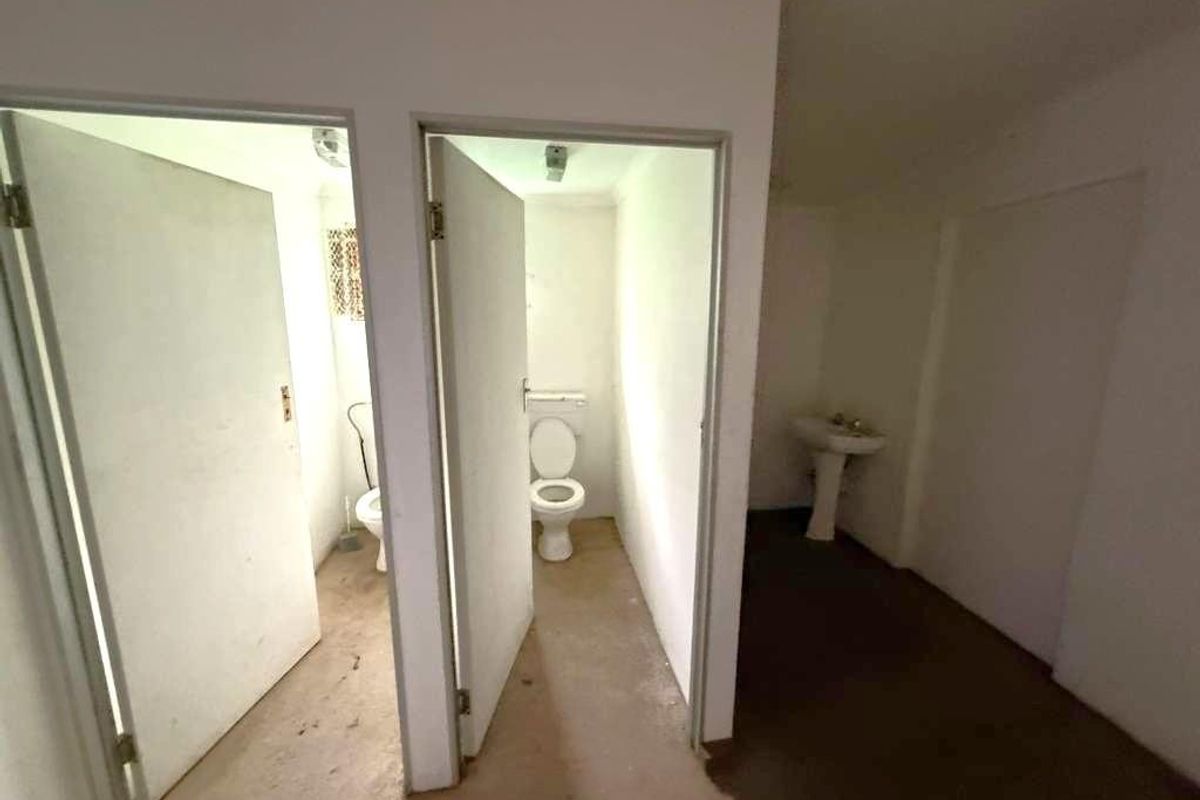 A basic industrial bathroom facility featuring two separate toilet cubicles and a pedestal basin in a dated, utilitarian space.