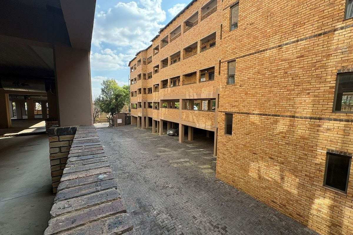 Exterior view of the apartment complex featuring a multi-story brick facade with covered parking bays and paved driveway access.