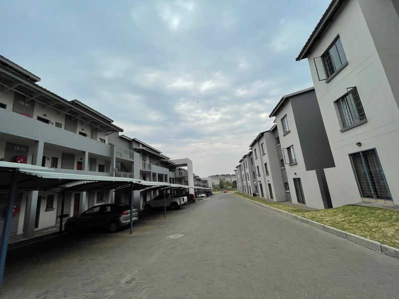 Exterior view of a modern apartment complex featuring paved driveways, covered parking bays, and multi-story residential buildings with contemporary finishes.