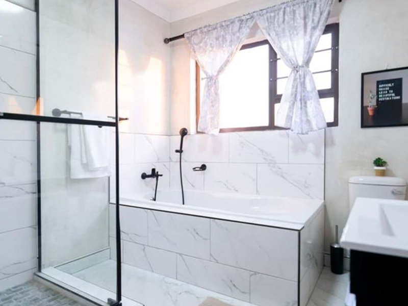 Modern bathroom featuring a glass-enclosed shower, a built-in bathtub with marble-look tiling, and contemporary black matte fixtures.