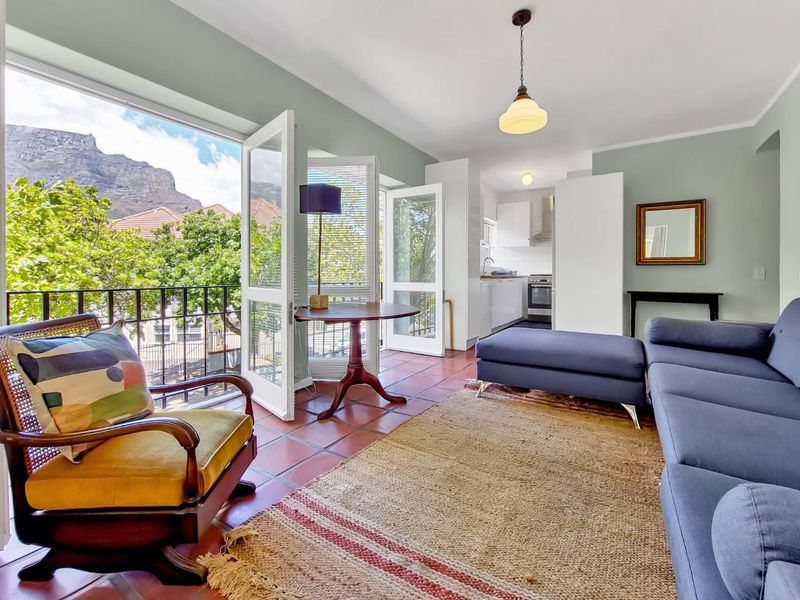 Bright open-plan living area featuring terracotta flooring, double doors opening to a balcony with mountain views, and an integrated kitchen space.