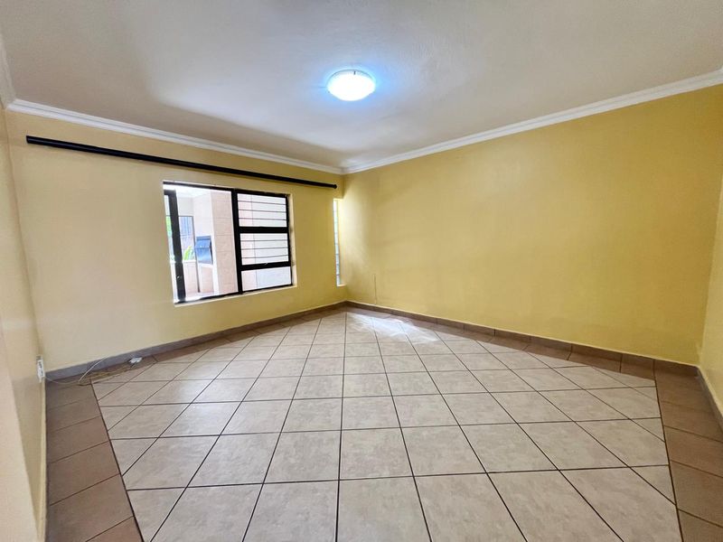 An empty living room featuring tiled flooring, neutral yellow walls, and aluminium window frames, offering a blank canvas for interior design.