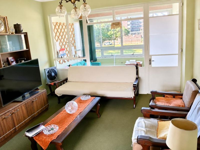 A living room featuring large windows, green carpeting, and a glass panel door leading to an outdoor area.