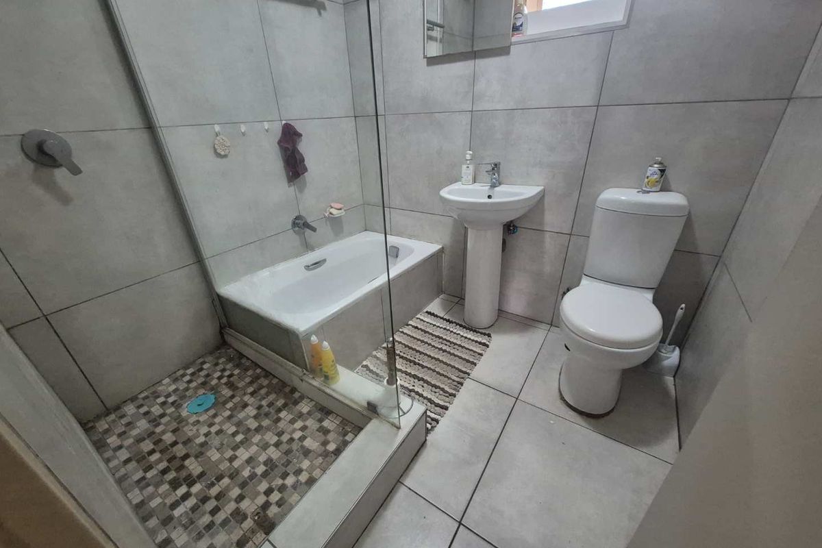 A modern bathroom featuring a glass-enclosed shower, a separate bathtub, a pedestal sink, and a toilet with neutral grey wall and floor tiling.