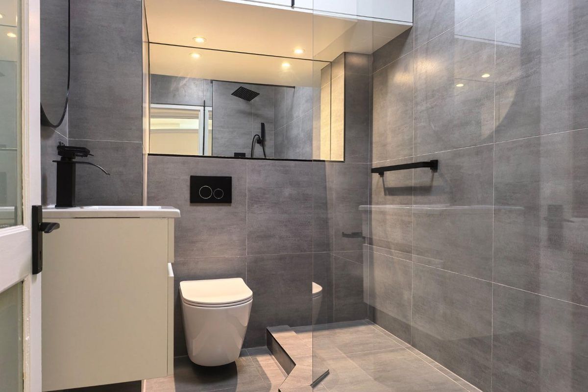 Modern bathroom featuring grey floor-to-ceiling tiling, a wall-hung toilet with concealed cistern, and a spacious walk-in shower with a glass screen.