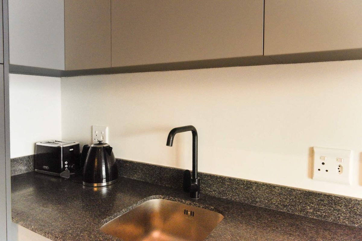 A modern kitchen area featuring sleek handleless cabinetry, a dark granite countertop, and a contemporary black gooseneck faucet with an undermount sink.