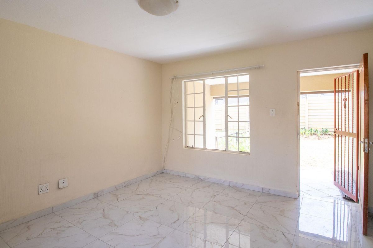 A bright, empty bedroom featuring modern marble-look floor tiles, a large window, and direct access to an outdoor area through a security gate.