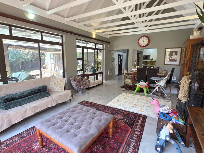 Spacious open-plan living and dining area featuring exposed timber ceiling beams, polished concrete floors, and large sliding glass doors providing ample natural light.