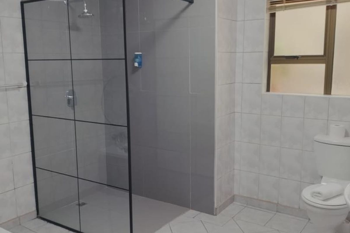 A modern bathroom featuring a walk-in shower with a black-framed glass screen, tiled walls, and a standard toilet.