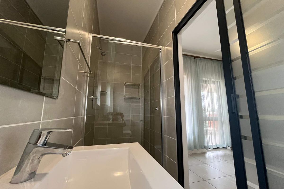 Modern bathroom featuring a glass-enclosed shower, wall-mounted basin with chrome fixtures, and neutral wall tiling, offering a clean and functional space.