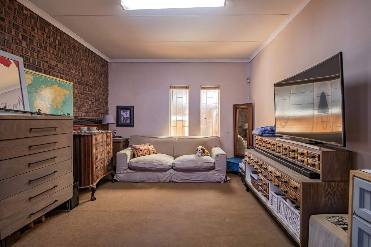 A living room featuring an exposed brick wall, neutral carpeting, and vertical windows, providing a functional space with potential for modern updates.