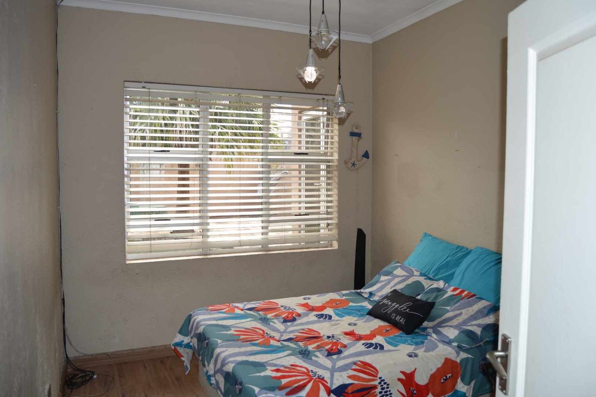 A bedroom featuring laminate flooring, a large window with fitted blinds, and modern pendant lighting.