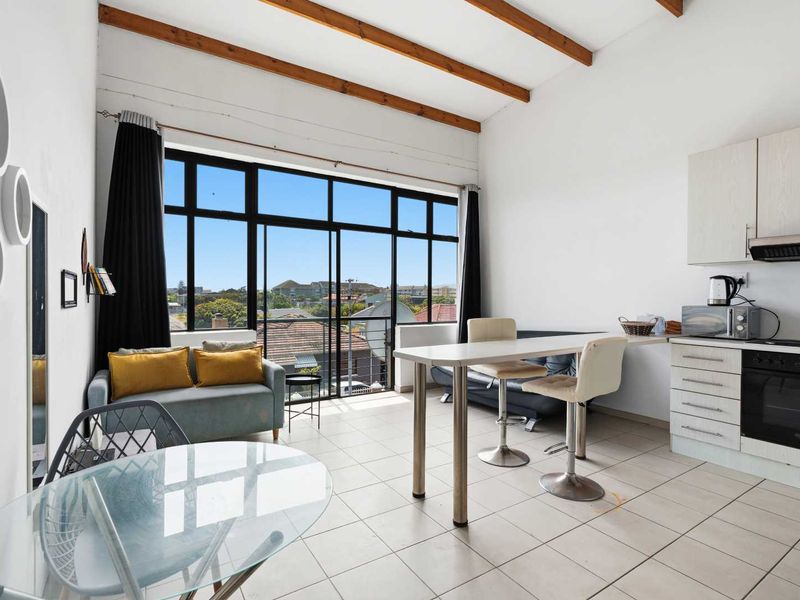 Open-plan living and kitchen area featuring exposed timber ceiling beams, tiled flooring, and large windows providing ample natural light and neighborhood views.
