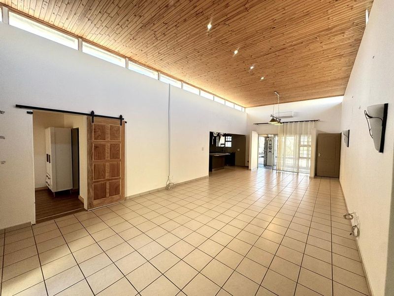 Spacious open-plan living area featuring a high timber-clad vaulted ceiling, clerestory windows for natural light, and neutral ceramic floor tiles throughout.