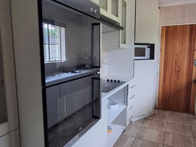 Functional kitchen featuring built-in oven, electric hob, extractor fan, and ample cabinetry with tiled flooring throughout.