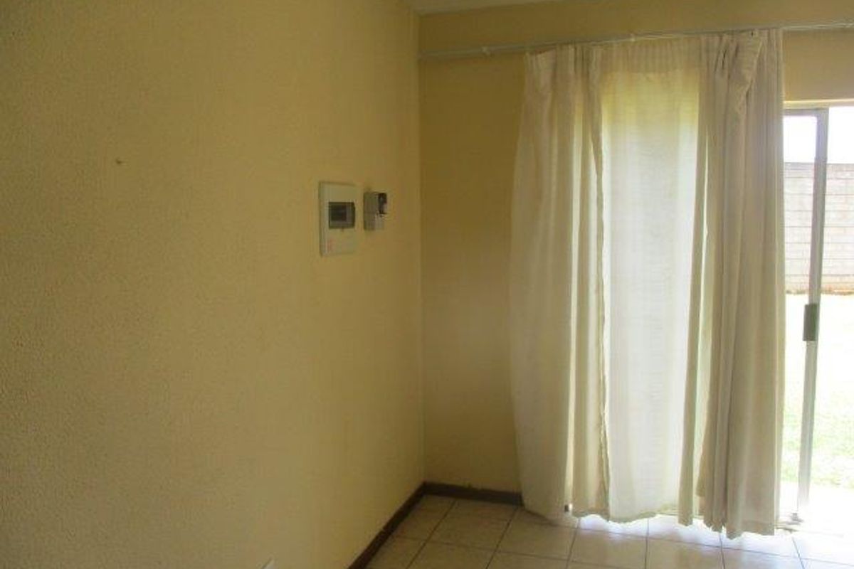 A simple living area featuring tiled flooring, a wall-mounted electrical distribution board, and a sliding glass door providing access to the exterior.