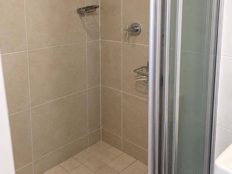 A clean, modern shower stall featuring neutral-toned wall and floor tiles, a glass enclosure, and a built-in shower mixer.